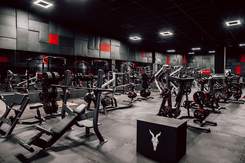Multiple fitness equipment standing in a gym with black floor, walls and ceiling.