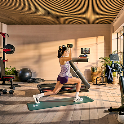 Model performing dumbbell lunges beside adidas T-700 Treadmill 