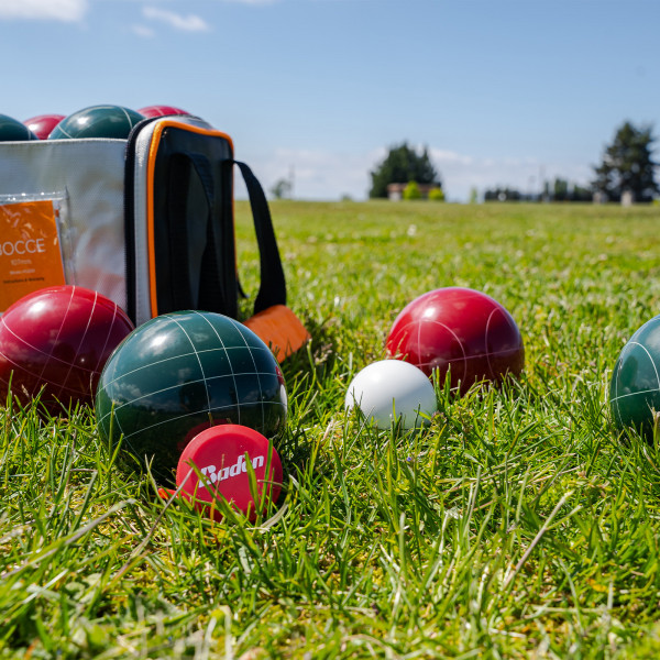 Close-up of bocce balls, pallino, measuring tape, and carry bag on grass.
