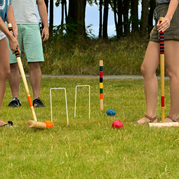 Group of people playing croquet on a grassy field.
