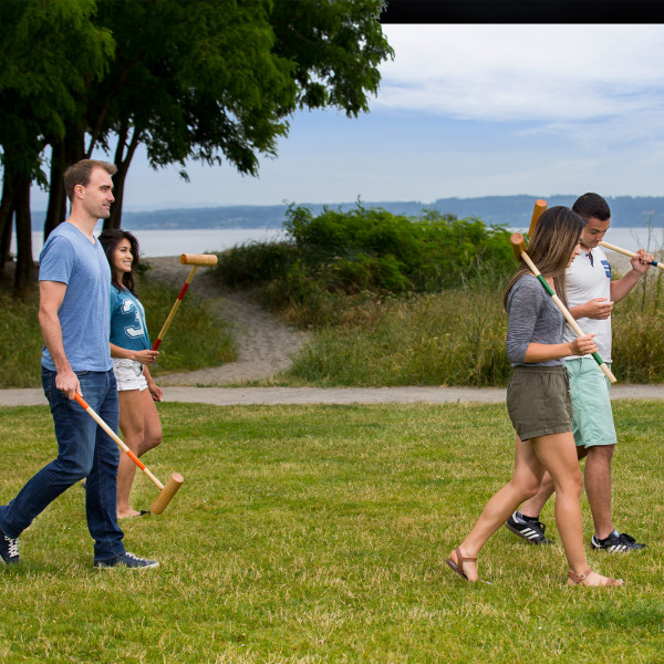 Group of people walking across the field carrying croquet mallets.