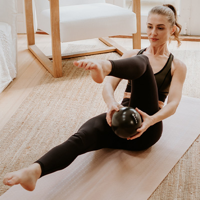 Image of a model passing the dark flowball underneath their leg whilst maintaining a sitting, balance exercise.