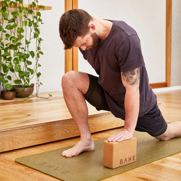 A lifestyle product image of the BAHE Cork Yoga Block with a model performing a leg stretch.