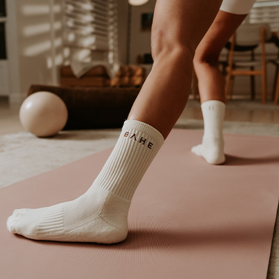 Image of the BAHE Studio Grippy Crew Socks being worn by a model standing on a yoga mat