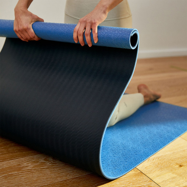 Person unrolling the BAHE Super Grip 6mm Mat showing both the textured top and grip underside in the Powder Blue colour variation.