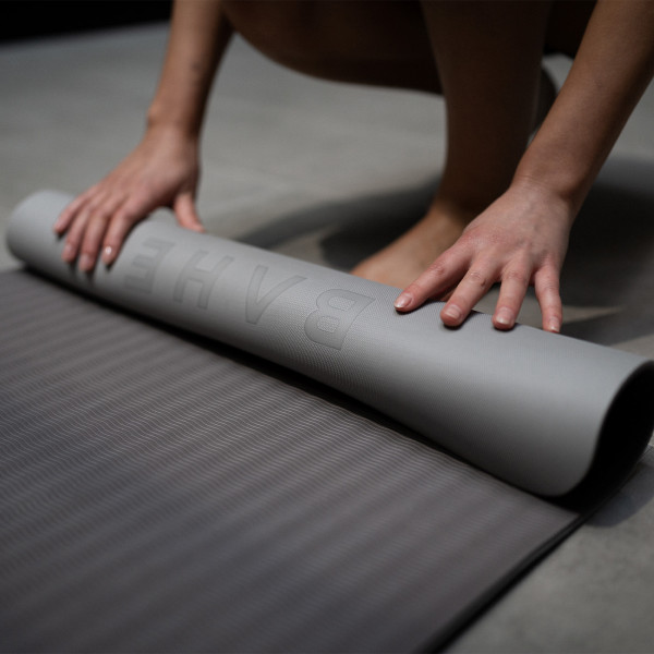 Person unrolling the BAHE Soft Touch Reversible XL 6mm Mat in the Pebble Grey colour variation.