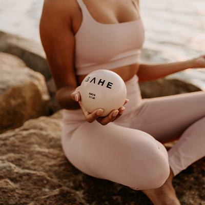 Photograph of a model sitting at the beach with the BAHE Toning Balls in hand