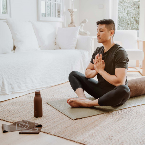 Lifestyle image of the BAHE Yoga Bolster being sat on by a model in a meditation pose
