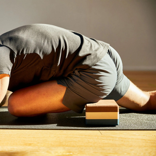 A lifestyle image of a model using the BAHE Yoga block during a deep leg stretch