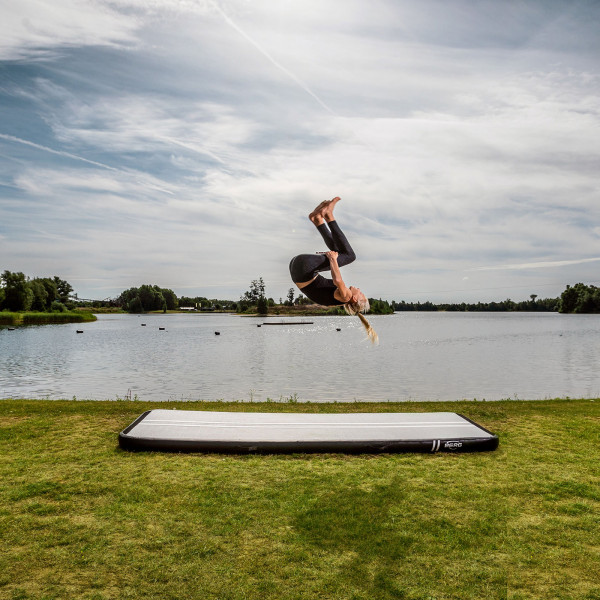 Athlete performing a backflip on BERG AirTrack Home by the lake.