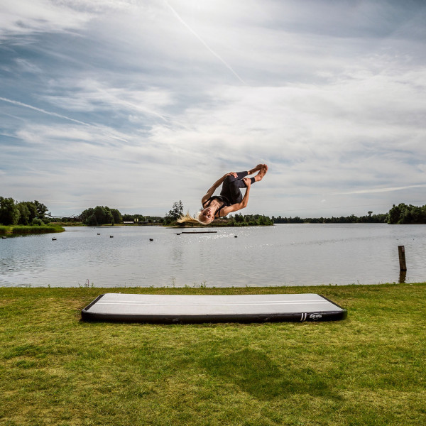 Athlete mid-air during a tuck flip on BERG AirTrack Home by the lake.