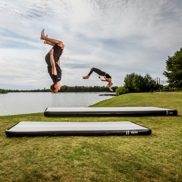Two athletes flipping in sync on BERG AirTrack Home by a lake