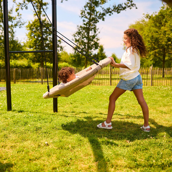 Toddler lying on the BERG PlayBase Nest Swing while being pushed by an older child