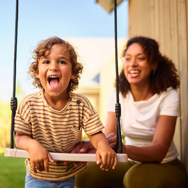 Smiling child on the BERG PlayBase Seat Swing with parent nearby
