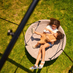 Two children lying together on a round swing on the BERG PlayBase