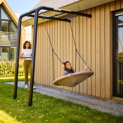 Child relaxing in a swing seat on the BERG PlayBase Wall with adult nearby