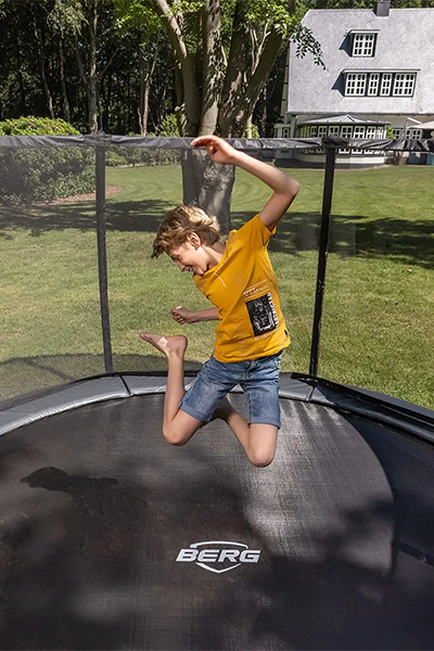 Action shot of the model jumping on the BERG Champion InGround Trampoline with Safety Net Deluxe