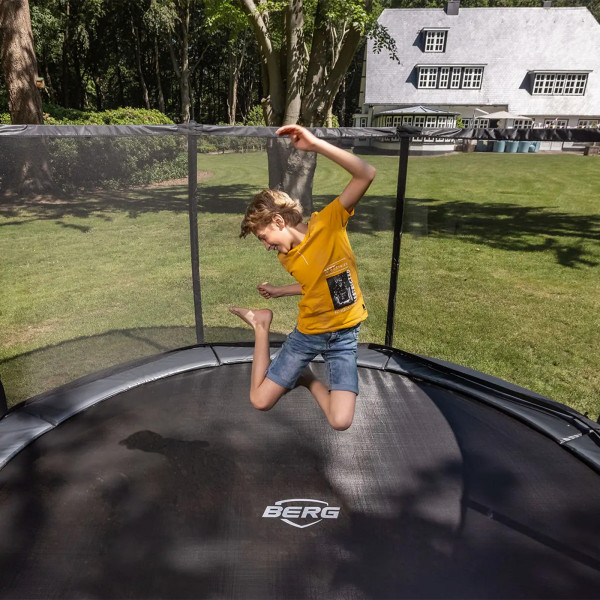 Action shot of the model jumping on the BERG Champion InGround Trampoline with Safety Net Deluxe