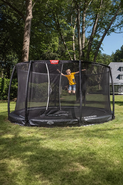 Wide shot of the model jumping on the BERG Champion InGround Trampoline with Safety Net Deluxe