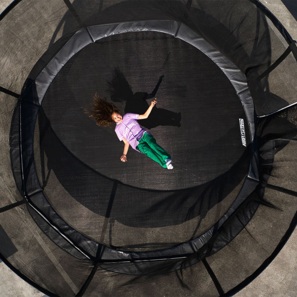 Top view shot of the model lying on the BERG Champion Regular Trampoline with Safety Net Deluxe