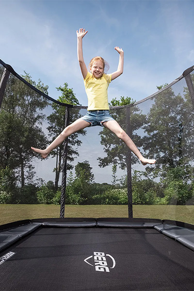 Action shot of the model jumping on the BERG Ultim Champion InGround Trampoline with Safety Net Deluxe