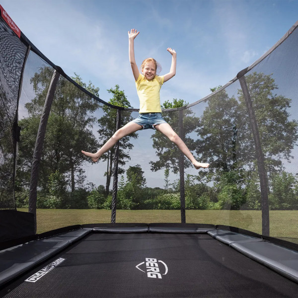 Action shot of the model jumping on the BERG Ultim Champion InGround Trampoline with Safety Net Deluxe
