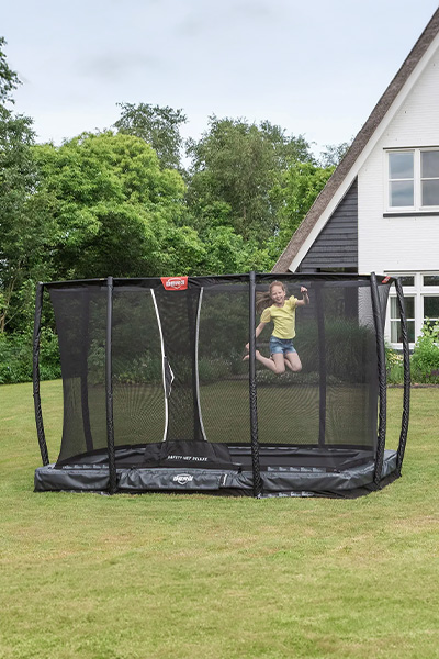 Wide shot of the model jumping on the BERG Ultim Champion InGround Trampoline with Safety Net Deluxe