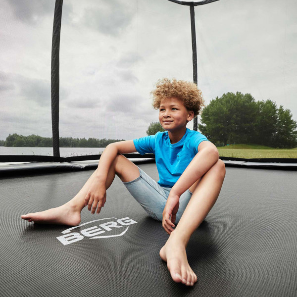 Model sitting on the BERG Ultim Champion Regular Trampoline with Safety Net Deluxe outdoors