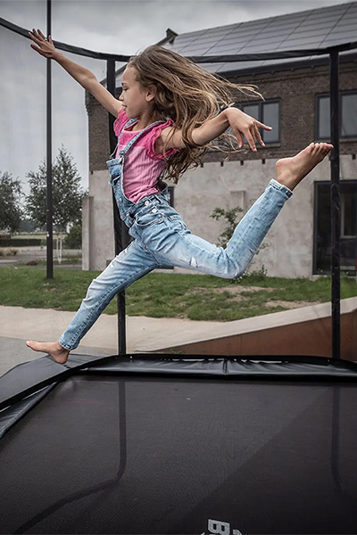 Action shot of the model performing a jump on the BERG Ultim Champion Regular Trampoline with Safety Net Deluxe