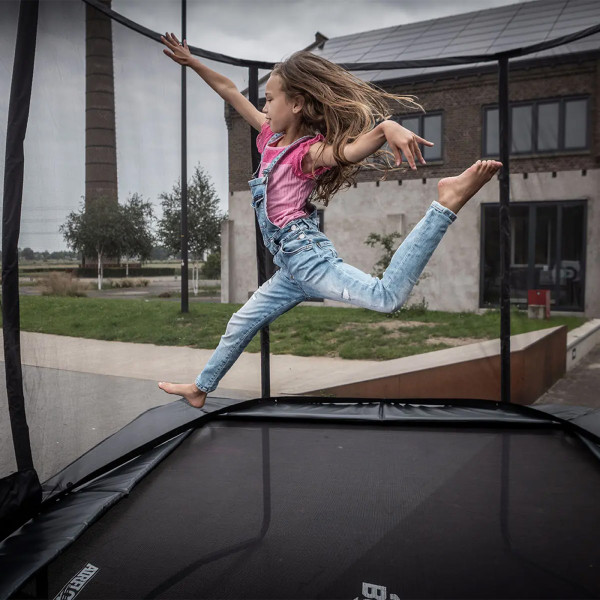 Action shot of the model performing a jump on the BERG Ultim Champion Regular Trampoline with Safety Net Deluxe