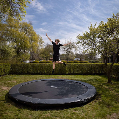 Model jumping on the BERG Sports Favorit Inground Trampoline in a garden