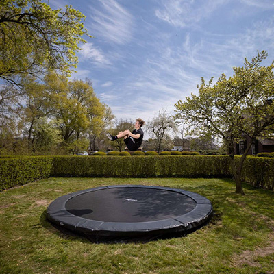Model performing a seated tuck jump above the BERG Sports Favorit Inground Trampoline