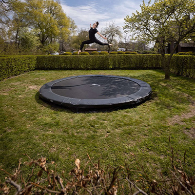 Model performing a straddle jump above the BERG Sports Favorit Inground Trampoline in a garden