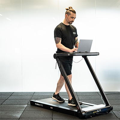Model walking on the BodyMax TM10 Walking Pad while using a laptop on the laptop tray
