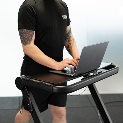Model walking on the BodyMax TM10 Walking Pad while using a laptop on the laptop tray 