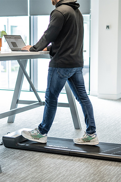 User walking on the BodyMax WP60 Treadmill while working at a desk