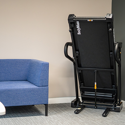 Folded BodyMax TM70 treadmill next to blue sofa
