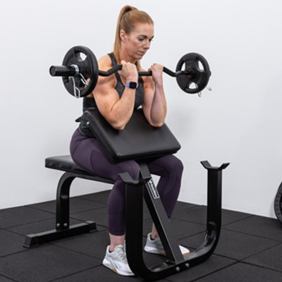 Lifestyle image of a model curling on the BodyMax CF625 Heavy Duty Preacher Curl Bench