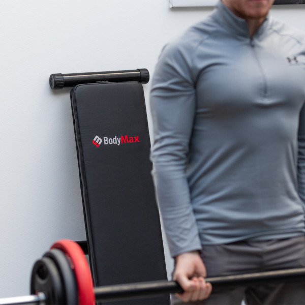 Image of the BodyMax CF306 Adjustable Abdominal Board / Sit Up Weight Bench folded behind a model performing a workout
