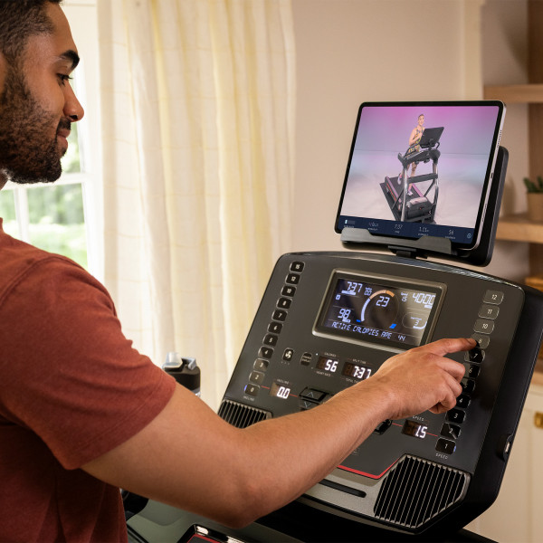 Person selecting a workout on the BowFlex T9 treadmill with a tablet on the console.