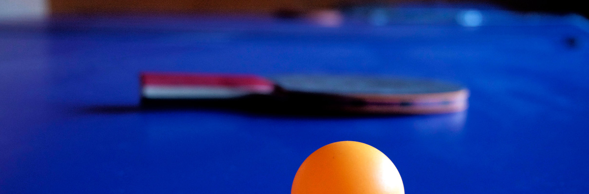 Orange table tennis ball on a blue table tennis table with a bat in the background