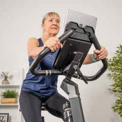 Lifestyle image of the cardiostrong BX60 Indoor bike. The model is riding the bike and watching the console.