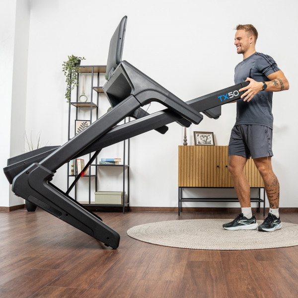 User folding the cardiostrong TX50 Treadmill in a home setting.
