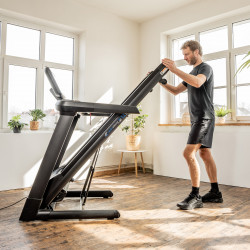 User folding the cardiostrong TX90 HD Smart Treadmill for storage.