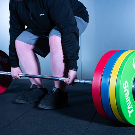 A person prepares to perform a deadlift with a Taurus Pro Barbell and brightly coloured Taurus weight plates.