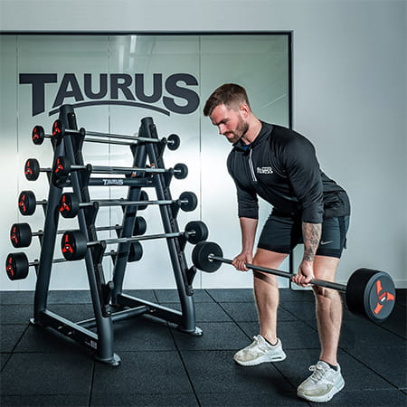 A person performing a barbell row with the Taurus Fixed Barbell