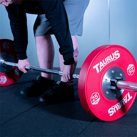 Person setting up for a lift with a barbell loaded with red Taurus 25kg Competition Olympic Bumper Weight Plates.