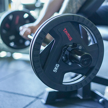 Close-up of the Taurus 5kg TPU Olympic Weight Plates loaded on a barbell during a workout.