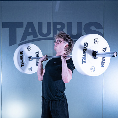 Person lifting a barbell with white Taurus 5kg Technique Bumper Weight Plates