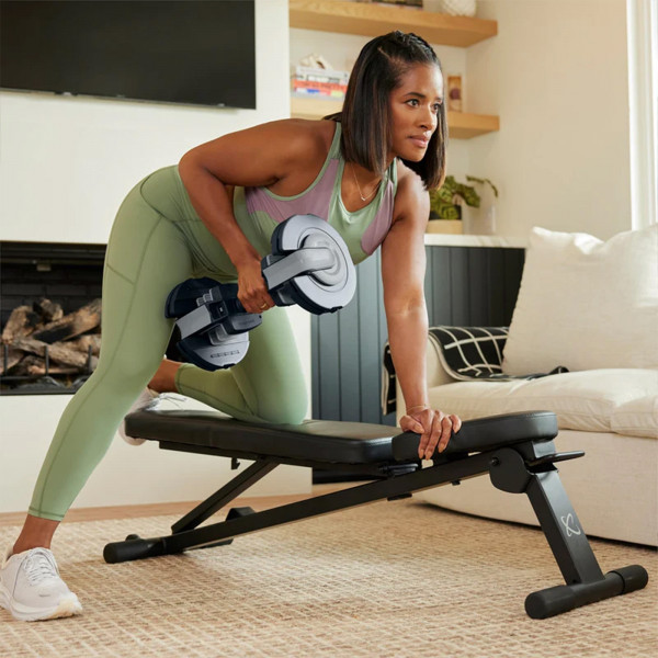 Person performing a one-arm row with the Centr Smart Stack 50 Adjustable Dumbbell on the Centr Folding Workout Bench.

